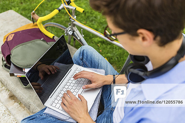 Young man with racing cycle sitting on a bench using laptop  elavated view