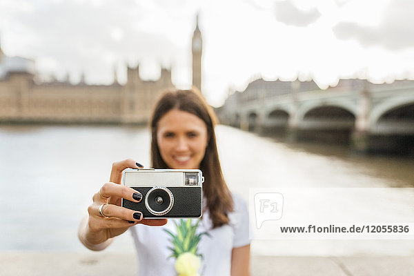 UK  London  woman holding old-fashioned camera near Westminster Bridge