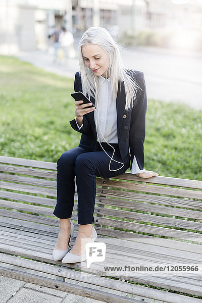 Junge Geschäftsfrau sitzt auf der Bank mit Handy und Kopfhörer