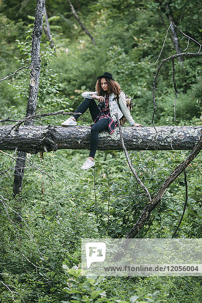 Teenage girl with camera sitting on deadwood in nature