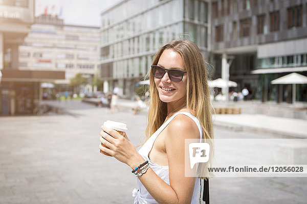 Lächelnde junge Frau mit Kaffee zum Mitnehmen in der Stadt