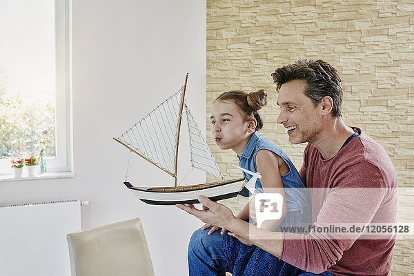 Happy father and daughter playing with model boat at home