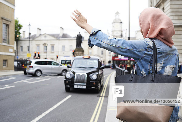 UK  England  London  junge Frau mit Hijab  die ein Taxi ruft