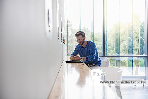 Smiling man looking at cell phone on table by the window