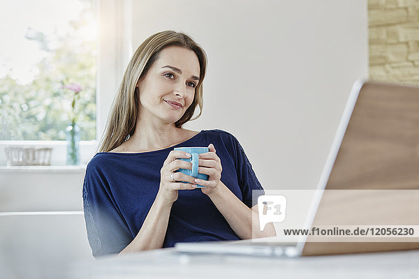 Frau zu Hause mit Kaffeetasse und Laptop