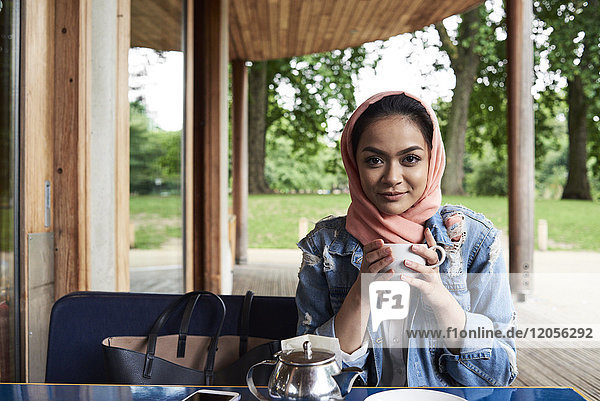 Junge Frau mit Hijab  die eine Tasse auf der Terrasse eines Cafés hält.