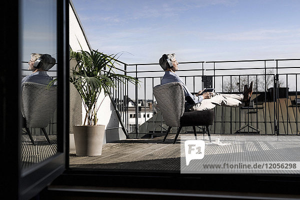 Grauhaariger Mann entspannt im Stuhl auf dem Balkon