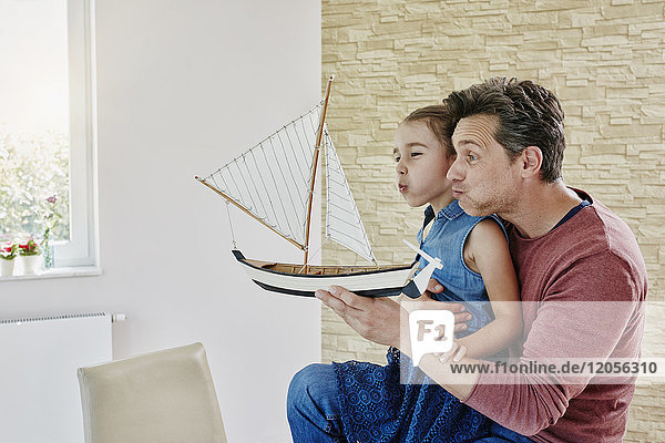 Happy father and daughter playing with model boat at home