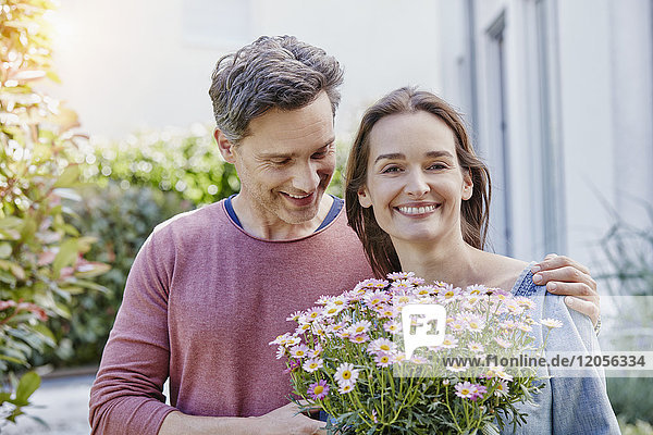 Portrait of smiling couple with flowers in front of their home