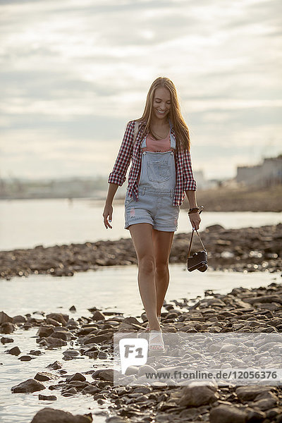 Young woman holding a camera walking on stony beach