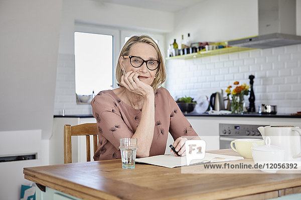 Porträt einer reifen Frau mit Notizbuch am Küchentisch