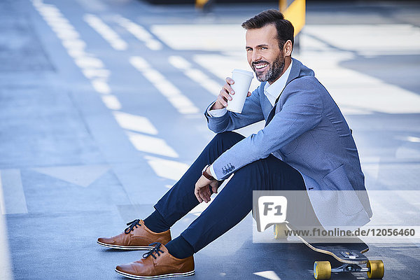 Geschäftsmann trinkt Kaffee und sitzt auf Longboard