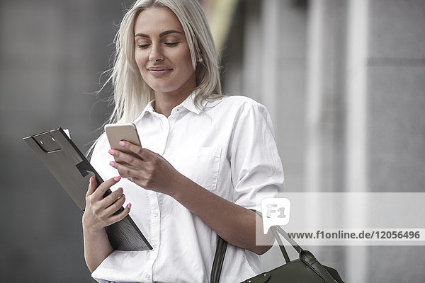 Smiling businesswoman with clipboard and cell phone outdoors