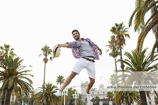 Spain  Barcelona  happy man jumping mid-air surrounded by palm trees