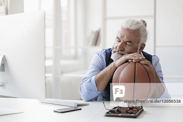Entspannter reifer Mann am Schreibtisch mit Basketball