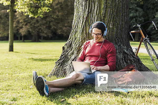 Mann mit Laptop und Kopfhörer im Park