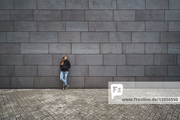 Young woman standing in front of grey facade waiting