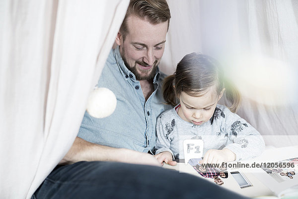 Vater und Tochter beim Betrachten des Fotoalbums im Spielzeug-Tipi