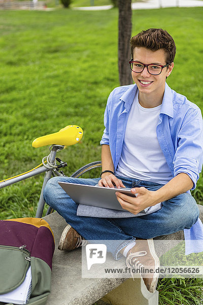 Portrait of smiling young man sitting on a bench using laptop