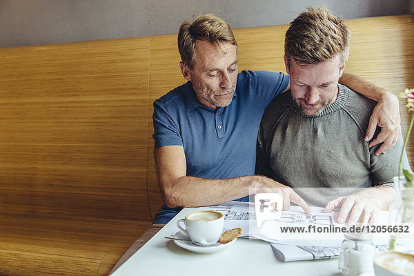 Gay couple looking at constructions plans for their home in cafe