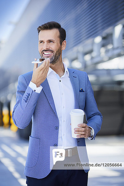 Porträt des lächelnden Geschäftsmannes mit Telefon und Kaffee in der Stadt