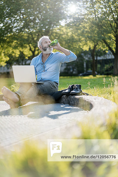 Erwachsener Mann trinkt Bier und benutzt Laptop im Park