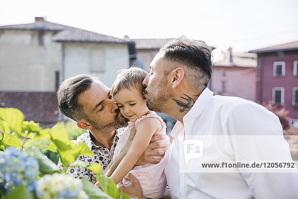 Schwules Paar  das seine Tochter im Garten küsst.