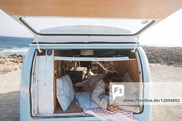 Spanien  Teneriffa  Frau mit Handy im Van am Meer geparkt