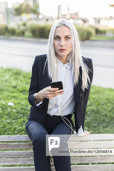 Junge Geschäftsfrau sitzt auf der Bank mit Handy und Kopfhörer