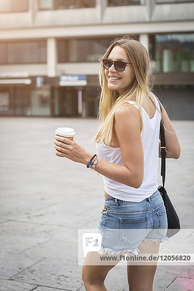 Lächelnde junge Frau mit Kaffee zum Mitnehmen in der Stadt