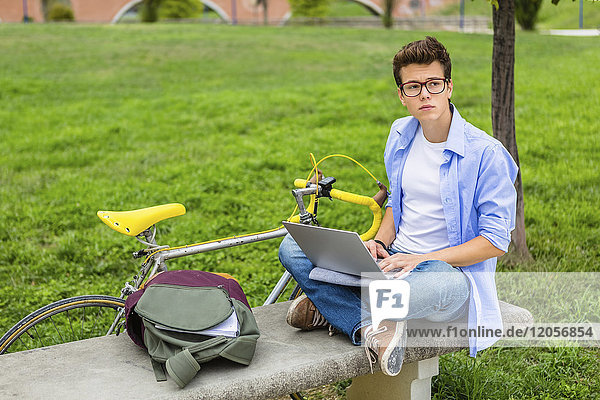 Pensive young man with racing cycle sitting on a bench using laptop