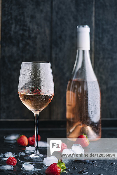 Glas gekühlter Rosenwein  Flasche  Eiswürfel und Erdbeeren und Himbeeren auf dunklem Boden