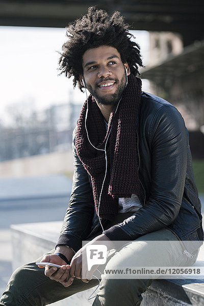 Smiling man with earphones listening to music on his smartphone