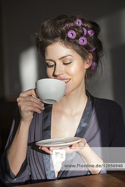 Junge Frau mit Lockenwicklern beim Kaffeetrinken
