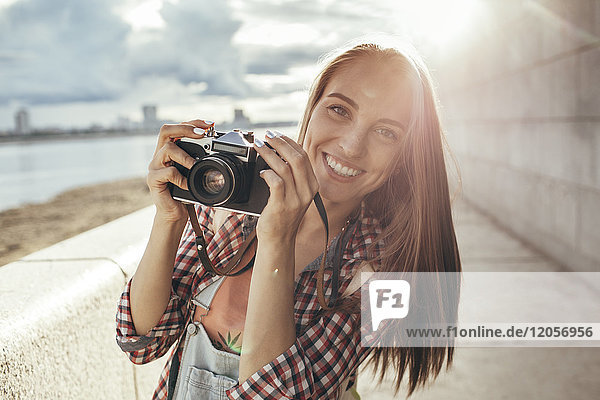 Lächelnde junge Frau mit Kamera am Flussufer