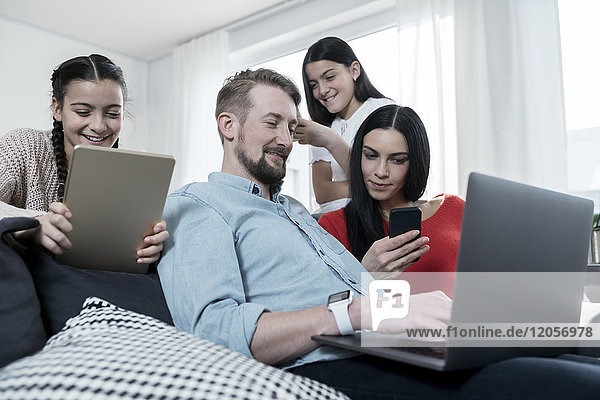 Parents and twin daughters on sofa using portable devices