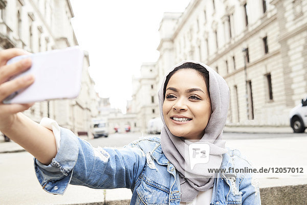 UK  England  London  junge Frau mit Hijab  die einen Selfie in der Stadt macht.
