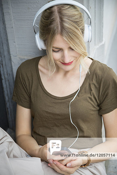 Entspannte junge Frau beim Musikhören mit Kopfhörer und Handy