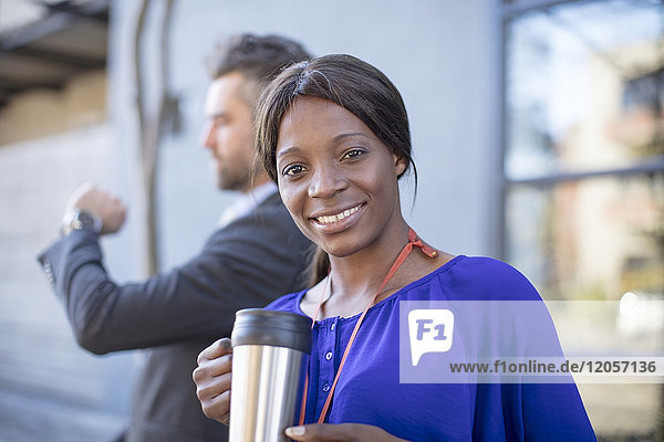 Portrait of smiling businesswoman with coffee mug and businessman in background
