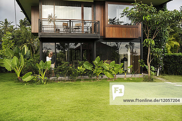 Gartenansicht des Paares in einem modernen Designhaus  umgeben von einem üppigen tropischen Garten.