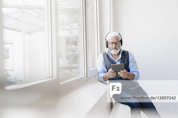 Erwachsener Mann mit Tablette und Kopfhörer am Fenster