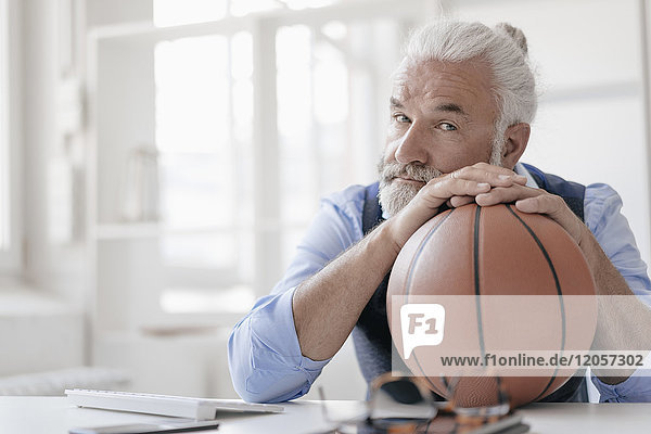 Porträt eines reifen Mannes am Schreibtisch mit Basketball