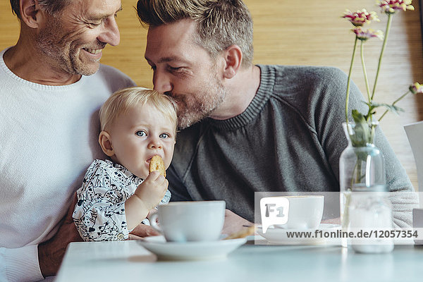 Schwules Paar kuschelt mit seinem Baby im Cafe