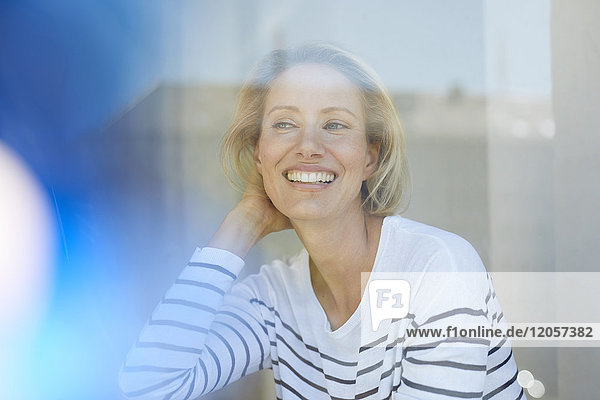Porträt der lachenden blonden Frau hinter der Fensterscheibe
