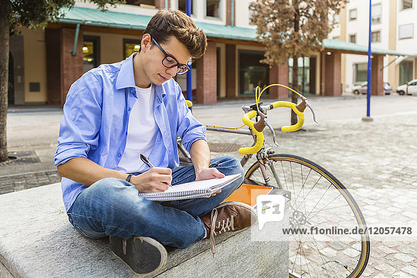 Junger Mann mit Rennrad auf der Bank sitzend  auf Notizblock geschrieben