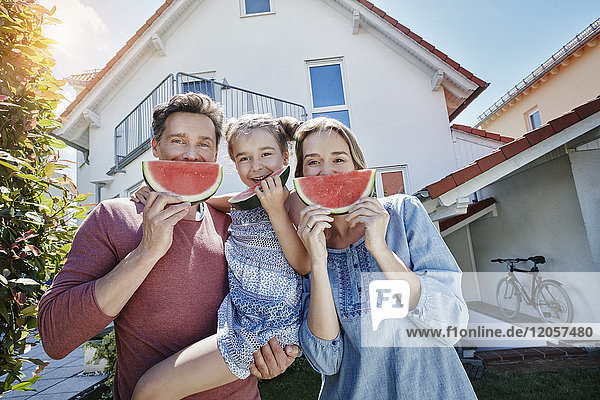 Portrait of happy family with slices of watermelon in front of their home