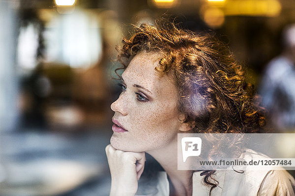 Portrait of pensive young woman behind windowpane