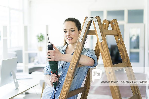 Portrait of woman at ladder holding electric drill