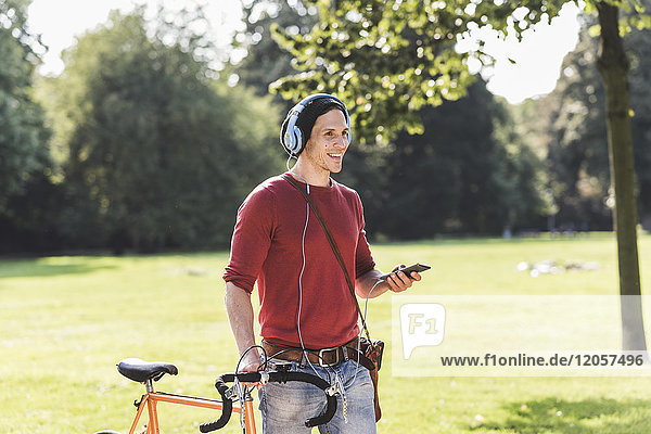 Lachender Mann mit Rennrad Musik hören mit Kopfhörern im Park