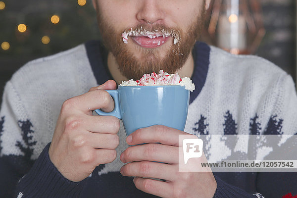 Mann trinkt heiße Schokolade mit Schlagsahne und gehackten Zuckerstangen zur Weihnachtszeit